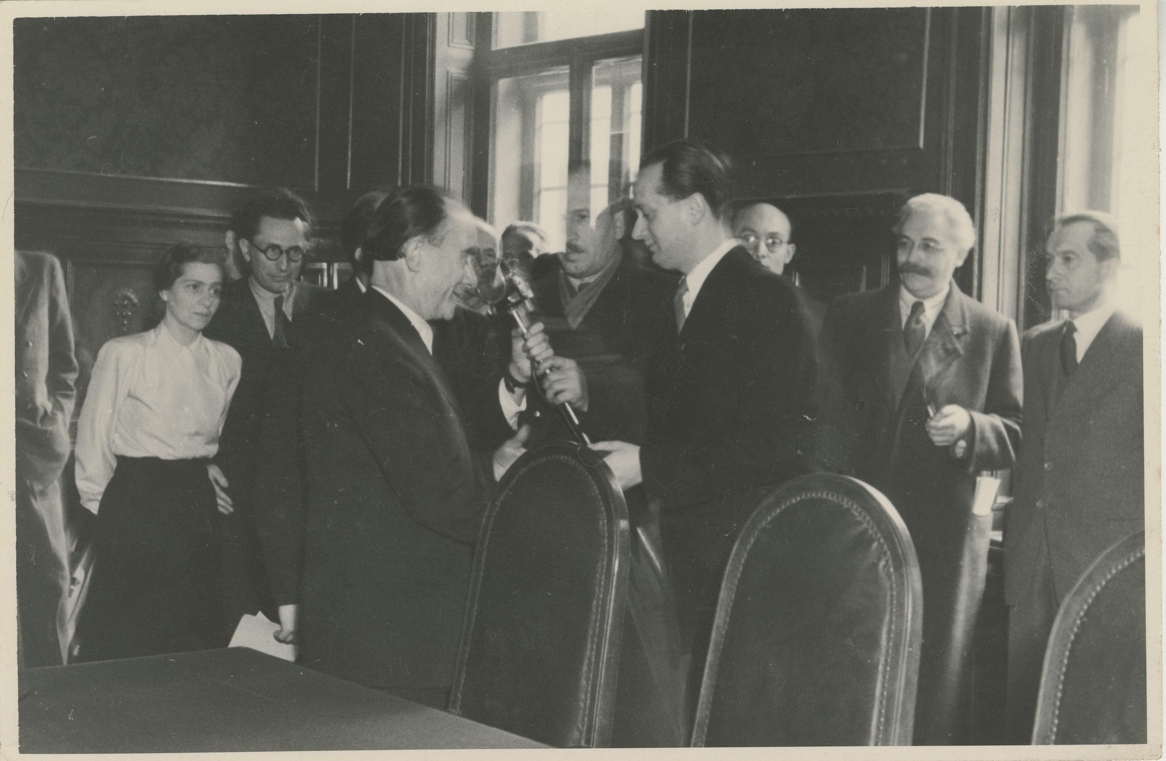 A Közoktatásügyi Minisztériumban Ortutay Gyula miniszter átadja a hatvan éves Kassák Lajosnak Ferenczy Béni erre az alkalomra készített plakettjét. Középen Kassák Lajos és Ortutay Gyula. A kép bal oldalán Kassákné Kárpáti Kláraé s Kardos László.